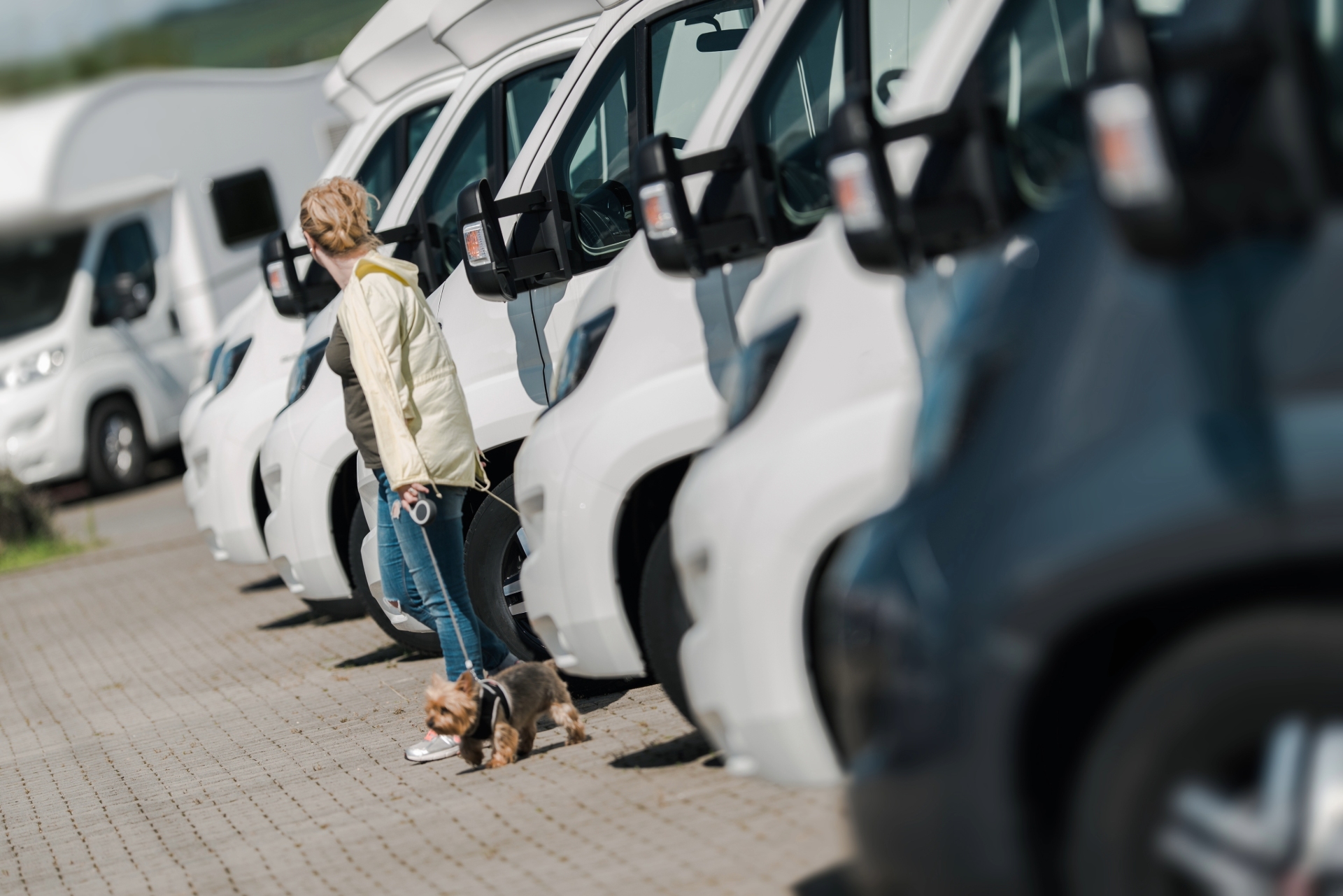 A woman standing in a row of RVs at a dealership with her dog on a leash.